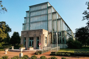 Front view of the Jewel Box, a stunning glass conservatory located in Forest Park, MO, surrounded by lush greenery.